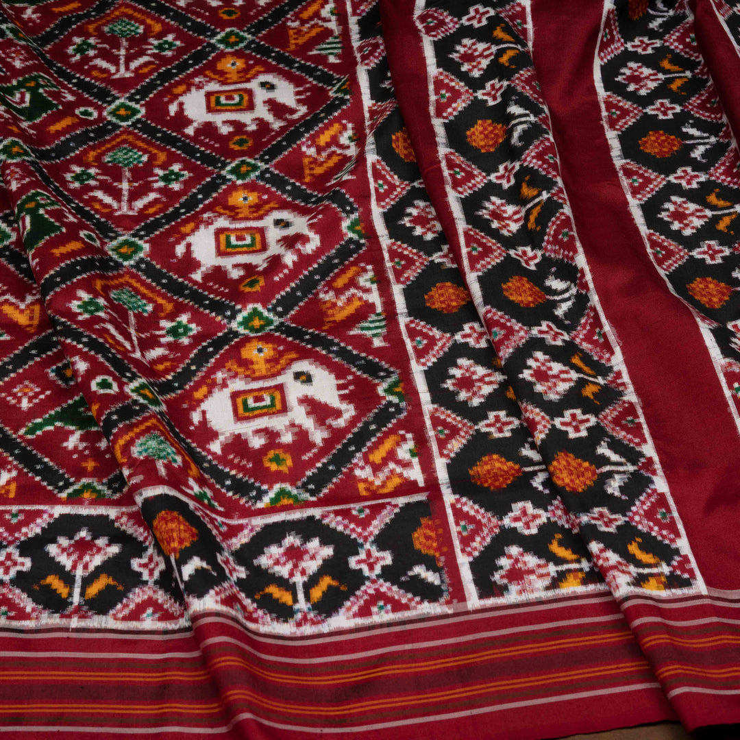 Traditional patterned fabric with elephants and geometric designs in red, black, and white.
