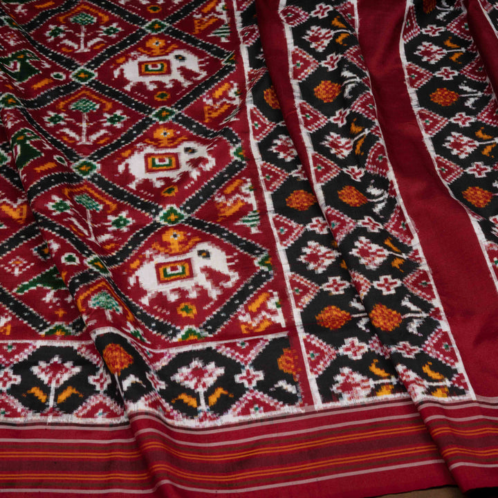 Traditional patterned fabric with elephants and geometric designs in red, black, and white.