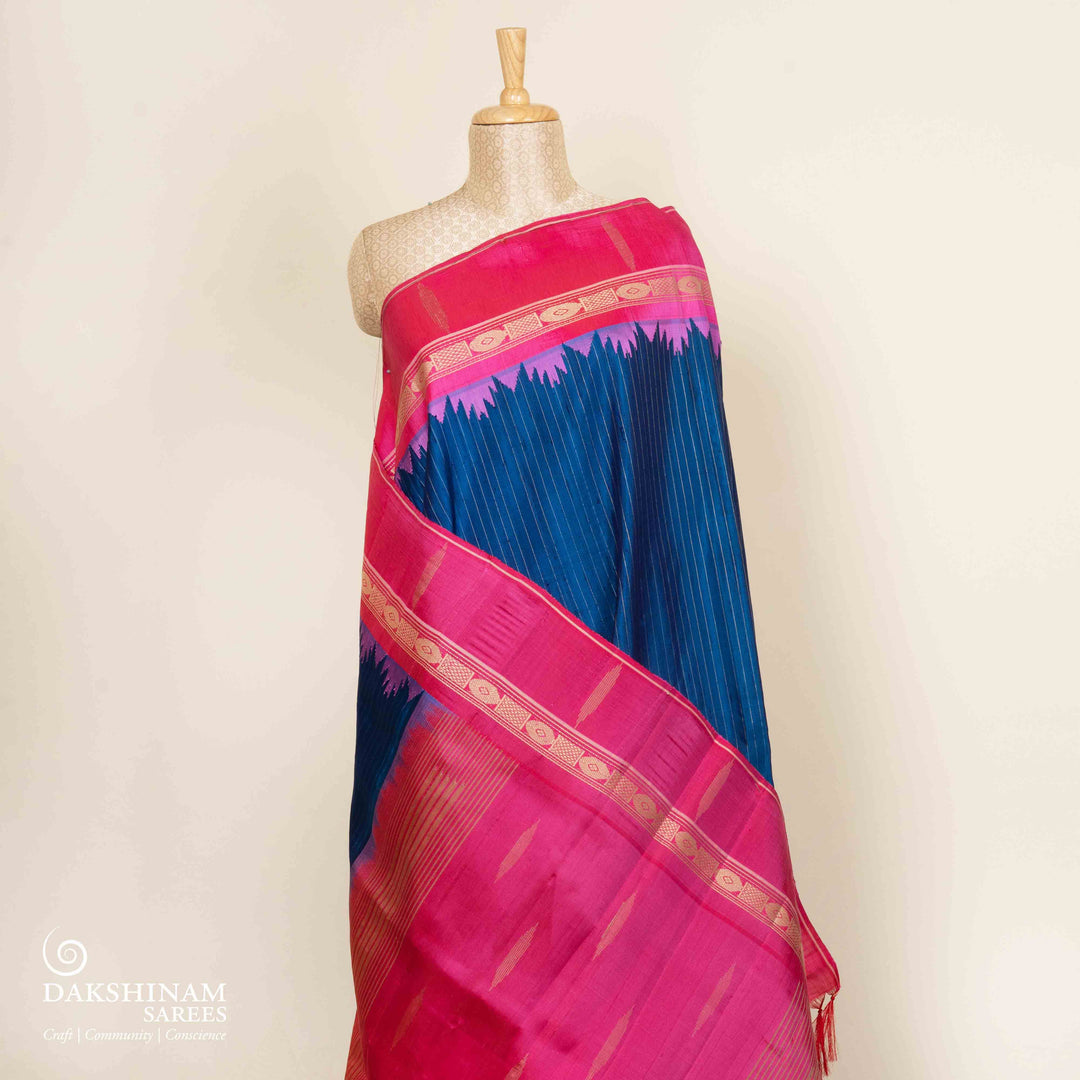 Blue Gadwal silk saree with raw silk finish body, silver stripe detailing, pink border with chakram and thazampoo motifs, pink blouse.