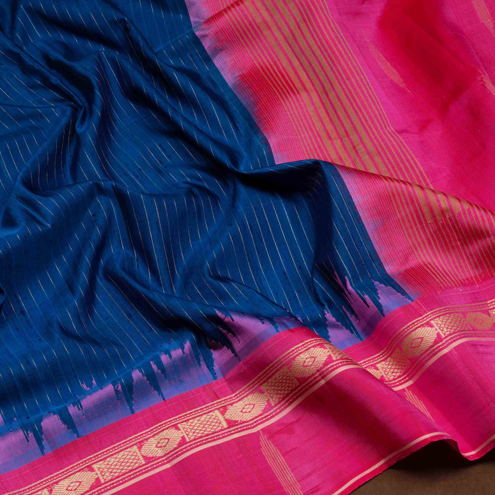 Blue Gadwal silk saree with raw silk finish body, silver stripe detailing, pink border with chakram and thazampoo motifs, pink blouse.