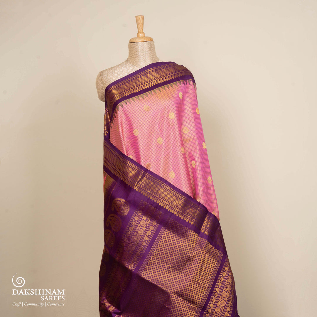 Dual tone pink and orange Gadwal silk saree with checkered body, purple zari border with rudraksh and temple motifs, plain purple blouse.