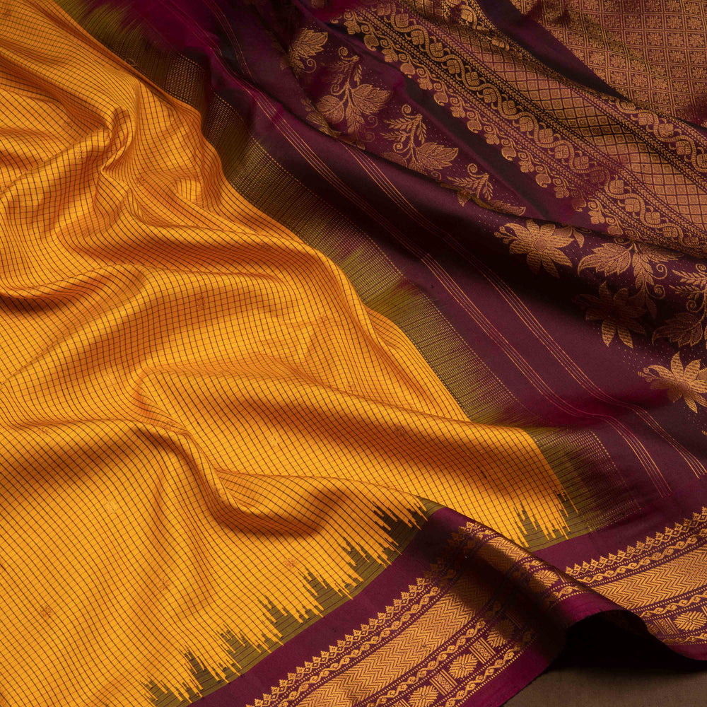 Yellow Gadwal silk saree with maroon checks and small butta body, maroon zari border with chakram and temple motifs, plain maroon blouse.
