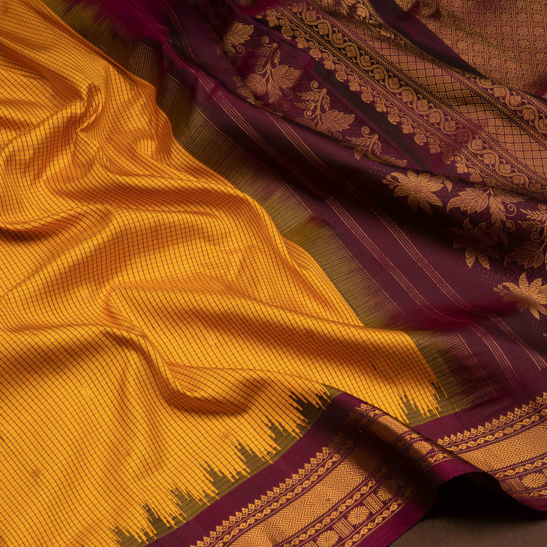 Yellow Gadwal silk saree with maroon checks and small butta body, maroon zari border with chakram and temple motifs, plain maroon blouse.