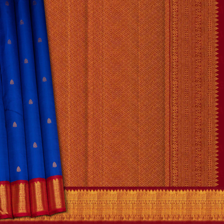 Blue handwoven Kanjivaram silk saree with gold buttas, red border with chevron and floral designs, and matching pallu, paired with plain red blouse.