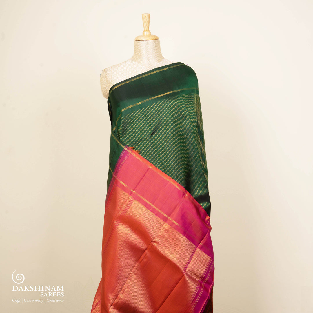 Green handwoven Kanjivaram silk saree with vertical gold dash buttas, rettapet border, and peach-pink dual tone pallu with zari motifs, paired with peach blouse.