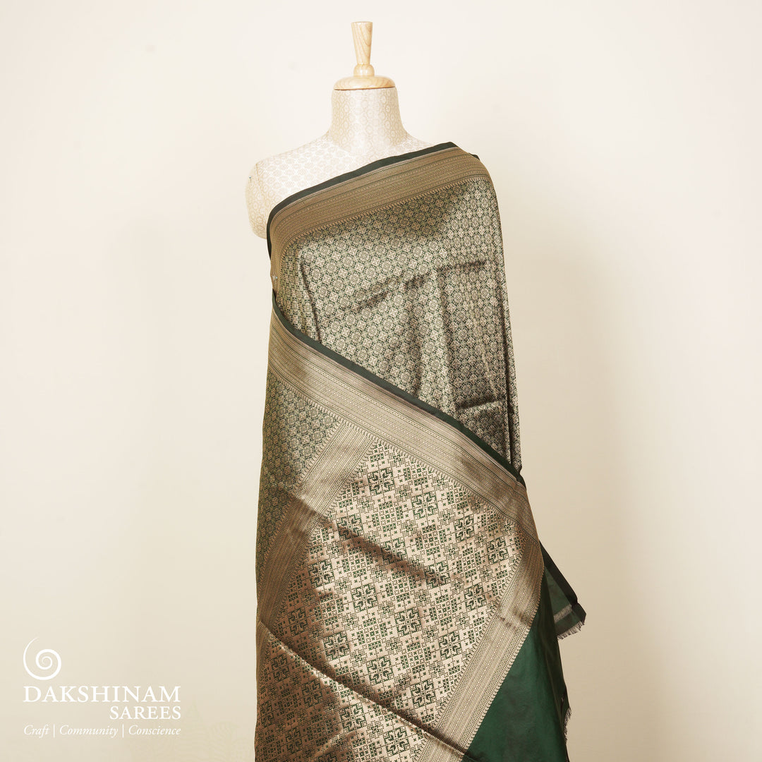 Dark green Banarasi silk saree with all-over gold brocade featuring round and diamond buttas, intricate zari border with chevron and traditional motifs, paired with a plain dark green blouse.