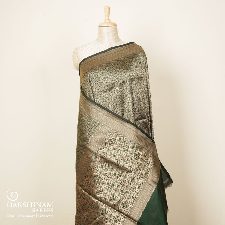 Dark green Banarasi silk saree with all-over gold brocade featuring round and diamond buttas, intricate zari border with chevron and traditional motifs, paired with a plain dark green blouse.