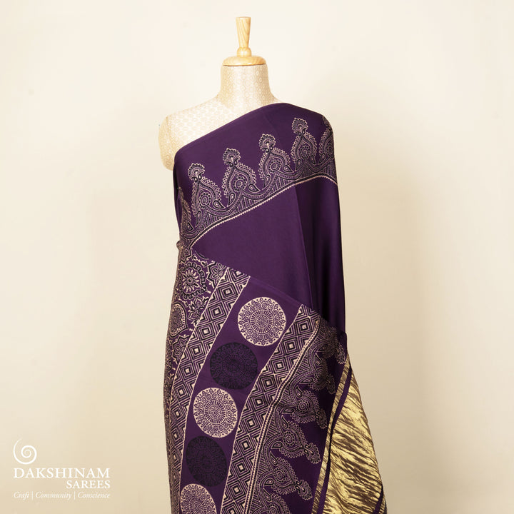 Violet handwoven modal silk saree with plain violet body, Ajrakh printed border, gold zari pallu, paired with a violet Ajrakh design blouse.