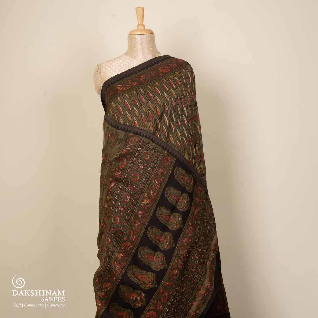 Army green handwoven Chanderi silk saree with yellow and red Ajrakh print, gicha temple border, floral pallu design, paired with green blouse with chevron lines.