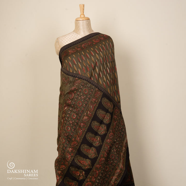 Army green handwoven Chanderi silk saree with yellow and red Ajrakh print, gicha temple border, floral pallu design, paired with green blouse with chevron lines.
