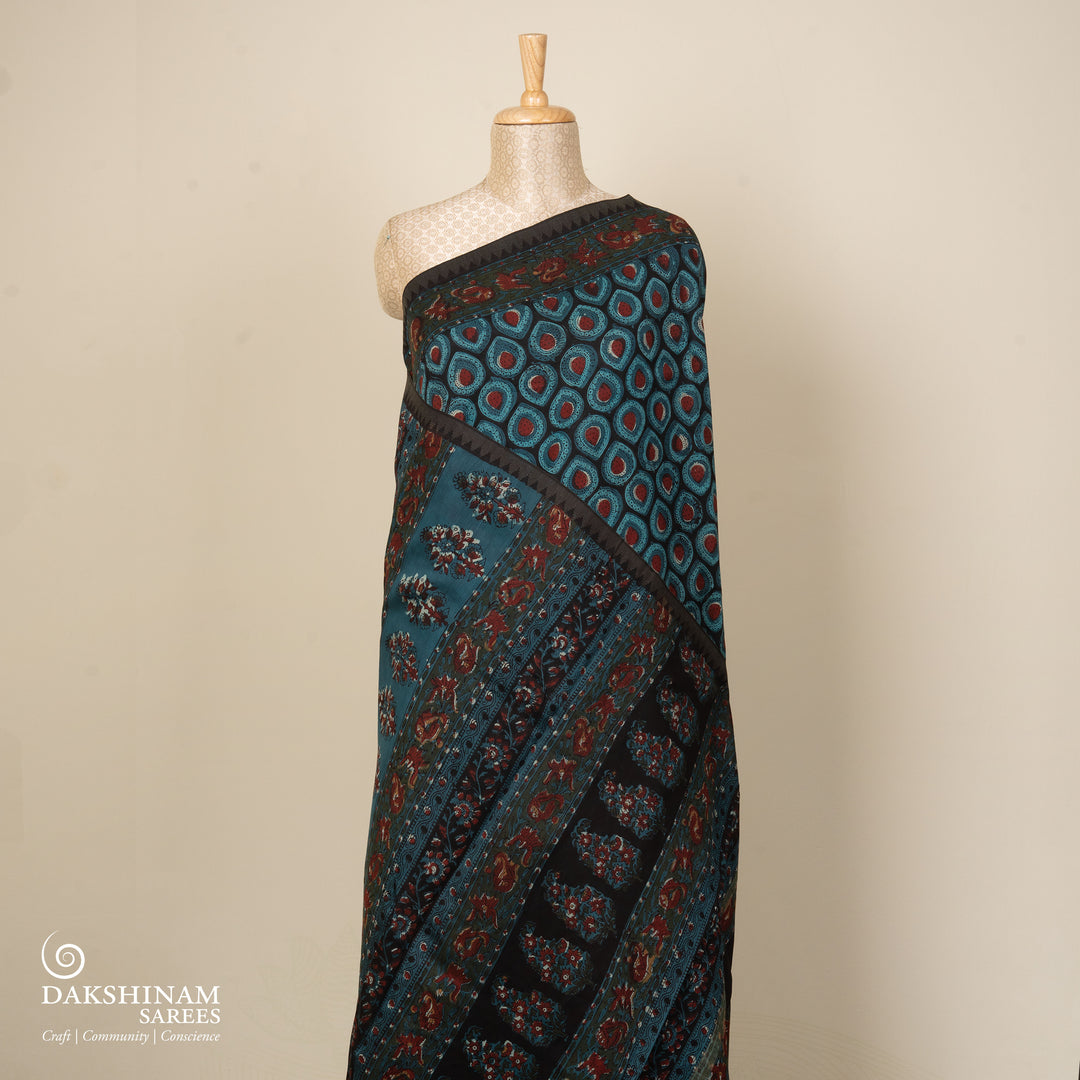 Blue handwoven Chanderi silk saree with Ajrakh print, gicha temple border, floral pallu design, paired with light blue blouse with chevron lines.