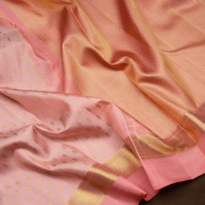 Light peach Kanjivaram silk saree with vairam buttas, peach pink border featuring temple and chevron designs, and detailed zari pallu, paired with plain blouse.