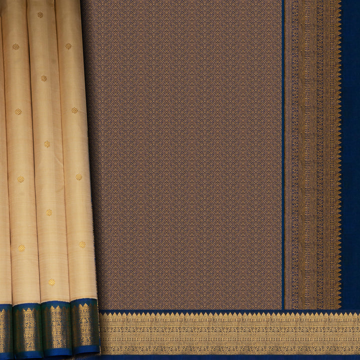 Cream Kanjivaram silk saree with chakram buttas, peacock blue border featuring chevron, rudraksham and floral lines, paired with plain blue blouse.