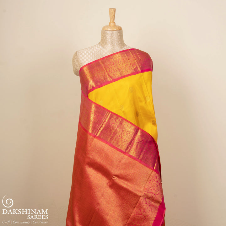 Yellow Kanjivaram silk saree with mayil buttas, pink korvai border featuring chakram and mango motifs, paired with plain pink blouse.