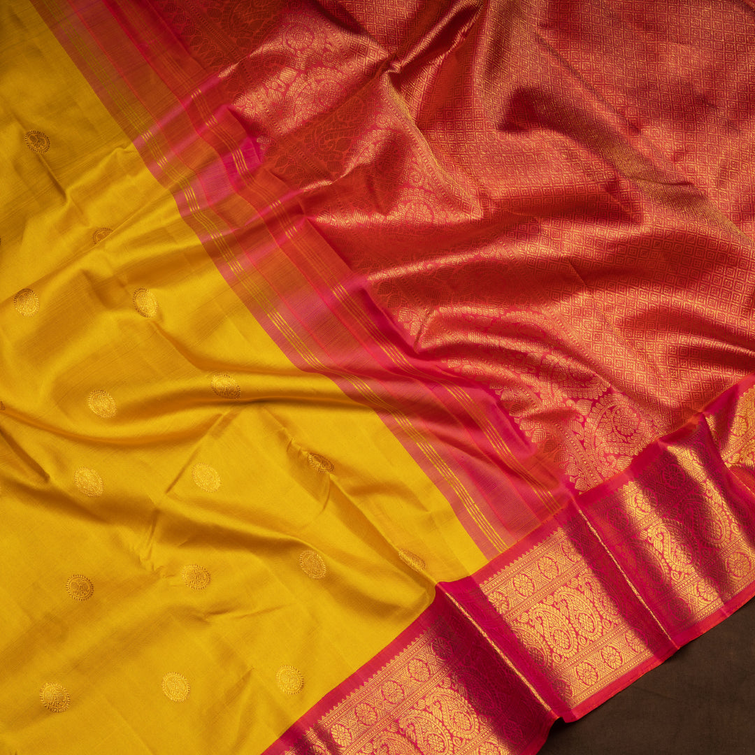 Yellow Kanjivaram silk saree with mayil buttas, pink korvai border featuring chakram and mango motifs, paired with plain pink blouse.