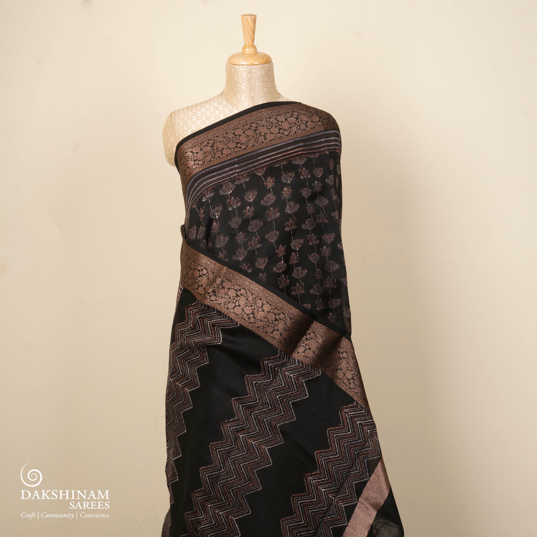 Black Chanderi silk cotton saree with white lotus floral print, gold zari border and orange striped pallu