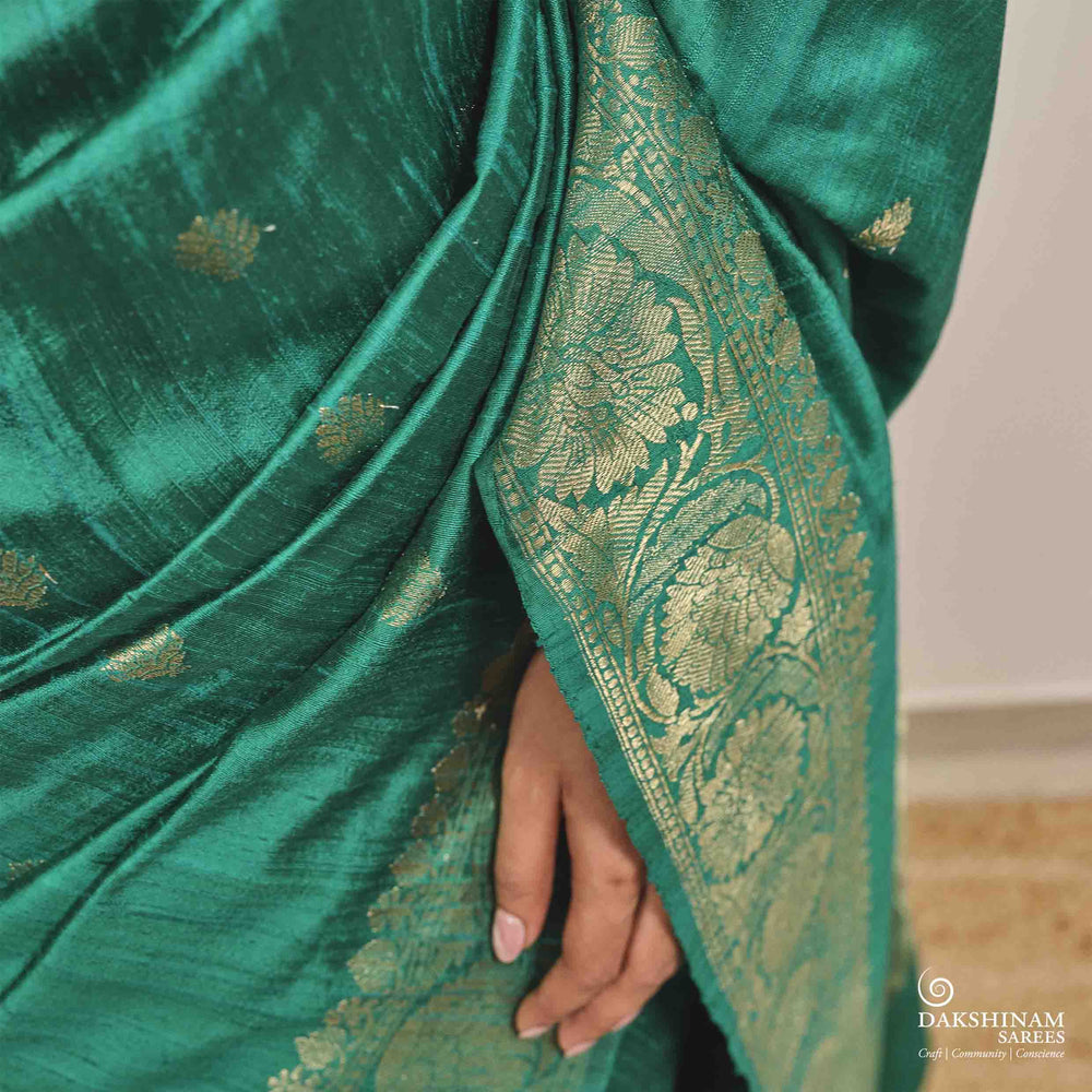 Green saree with gold patterns held by a hand, brand 'Dakshinam' visible