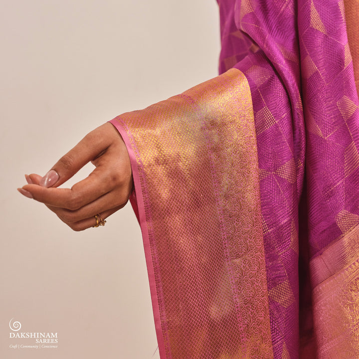 Close-up of a hand holding a purple and gold saree with 'Dakshinam' branding.