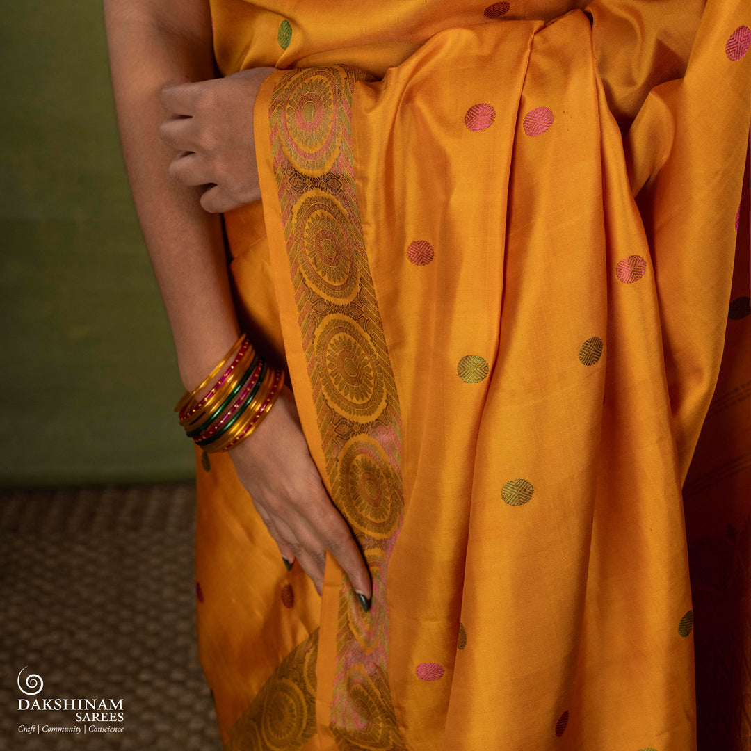 Yellow Kanjivaram silk saree with multicolor zari, red and green rudraksham buttas, green and red chakram border, floral pallu and plain yellow blouse with running border.
