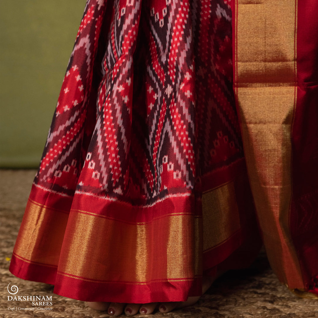 Red Ikat saree featuring maroon and grey diamond-shaped designs, gold zari border, chevron panel pallu with temple design, paired with a plain red blouse.