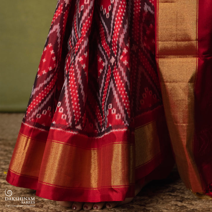 Red Ikat saree featuring maroon and grey diamond-shaped designs, gold zari border, chevron panel pallu with temple design, paired with a plain red blouse.