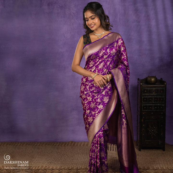Magenta and violet mixed Banarasi silk saree with gold zari floral buttas, beige leaf panel border and matching beige leaf panel pallu, paired with a magenta-violet blouse with beige leaf border.