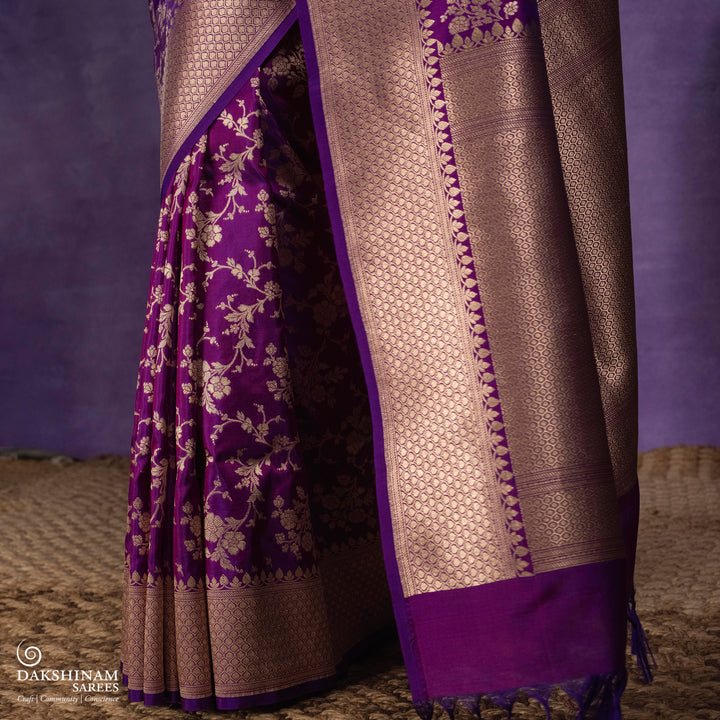 Magenta and violet mixed Banarasi silk saree with gold zari floral buttas, beige leaf panel border and matching beige leaf panel pallu, paired with a magenta-violet blouse with beige leaf border.