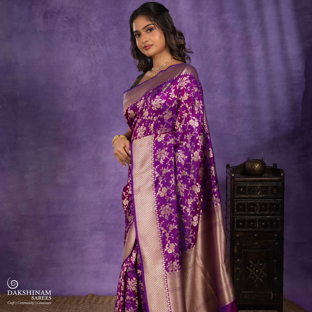 Magenta and violet mixed Banarasi silk saree with gold zari floral buttas, beige leaf panel border and matching beige leaf panel pallu, paired with a magenta-violet blouse with beige leaf border.