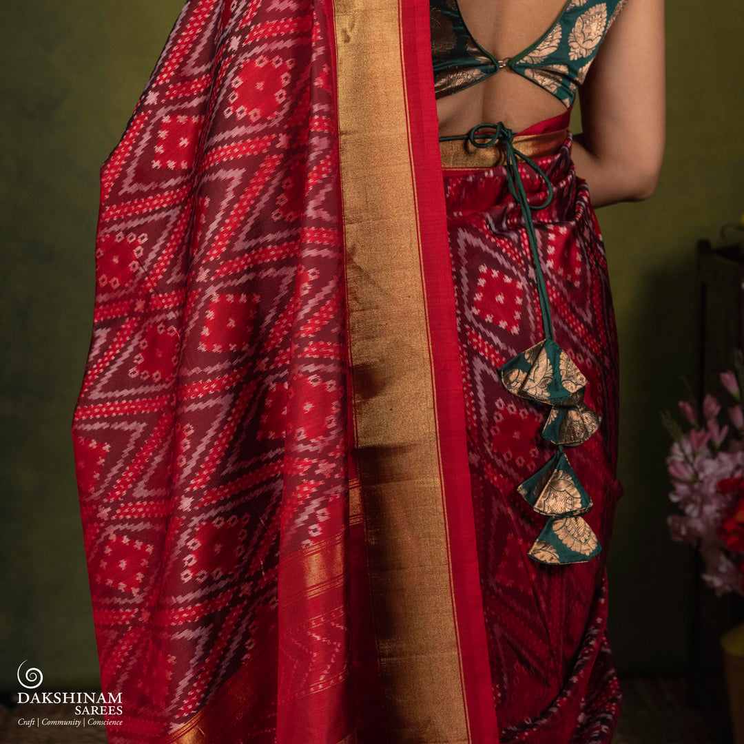 Red Ikat saree featuring maroon and grey diamond-shaped designs, gold zari border, chevron panel pallu with temple design, paired with a plain red blouse.