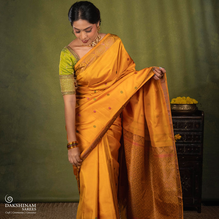 Yellow Kanjivaram silk saree with multicolor zari, red and green rudraksham buttas, green and red chakram border, floral pallu and plain yellow blouse with running border.